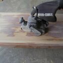 Using a belt sander to remove the finish and stain from a coffee table top.