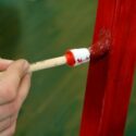 Brushing on bright red enamel paint on a old wooden school desk.