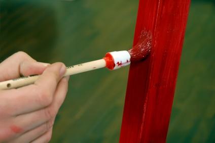 Brushing on bright red enamel paint on a old wooden school desk.