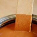 Wooden mixing stick partially submerged in new can cinnamon tinted wood stain.