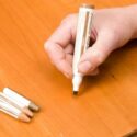 Using a furniture repair marker and putty sticks to fix a scratched cherry table surface.