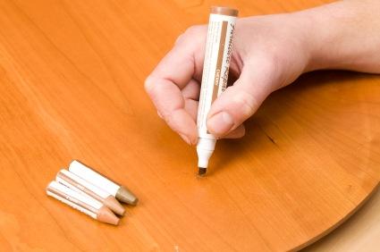 Using a furniture repair marker and putty sticks to fix a scratched cherry table surface.