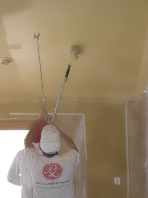 Spraying then back-rolling interior ceiling paint.
