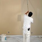 Applying paint with a roller to an interior room.