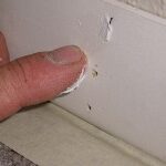 Filling nail holes with spackling paste in interior base trim.