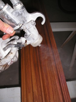 Applying a clear finish to a piece of wood trim using an HVLP sprayer.