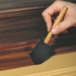 Applying glaze with a sponge brush before making a faux oak wood graining effect.