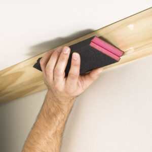 Hand sanding wood baseboard with a sanding sponge for a smooth finish.