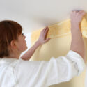 A young woman hanging wallpaper.