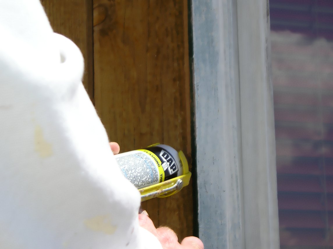 Applying brown colored caulk to cedar siding prior to staining.