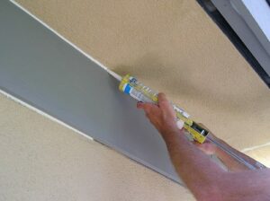 Using a caulking gun to apply caulking to exterior wood trim to stucco.