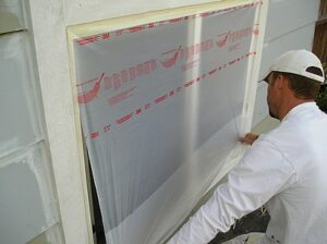 Spreading and pulling down plastic masking film applied to a window frame.