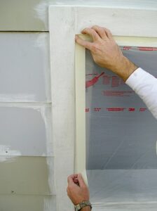 Securing plastic masking film with tape to a window frame.