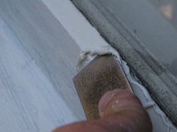 Applying glazing compound with putty knife to glass and wood window frame.