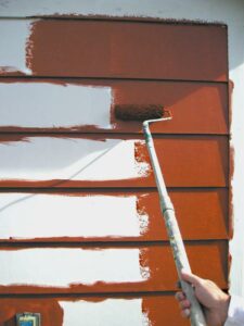 Using a paint roller to apply paint to wide masonite lap siding.