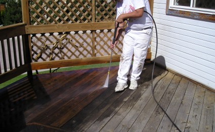 A painter using a pressure washer to wash or clean a wood deck.