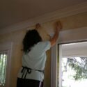 A woman stripping wallpaper and removing the glue.