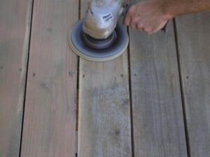 A large grinder with a sanding disc is used to sand a wood deck.