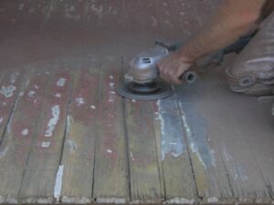 Large powerful disc grinder with sander attachment removing paint from T&G floor boards.