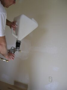 Using a hopper-gun to apply orange peel drywall texture.