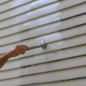 Painting the lap siding of a home with a brush.