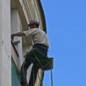 House painter suspended using a birds nest platform to paint a window.