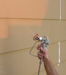 Correctly holding a airless spray gun while painting masonite siding.