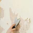 Removing the wallpaper backing material from a wall using a broad putty knife.