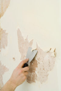 Using a putty knife to remove wallpaper backing paper.