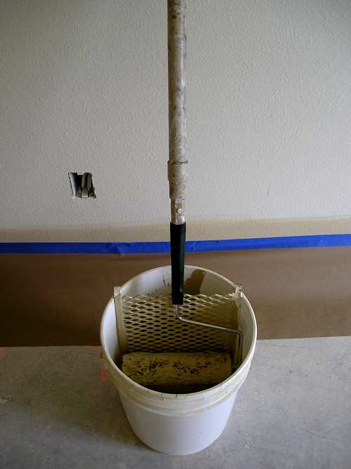 A 5 gallon paint bucket with grid and paint roller ready for painting.