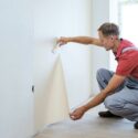 A man bent down hanging wallpaper.