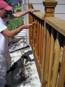 Applying deck stain to wood handrails using a brush.