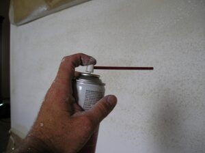 Using a spray can to apply orange peel drywall texture to a small patch.