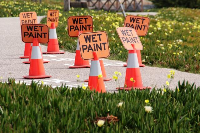 A group of wet paint signs and safety cones om a sidewalk..