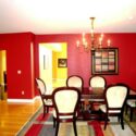 A dining area painted with a red wall, hardwood floor and white ceiling and trim.