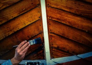 A man applying wood stain to T&G wood ceiling.