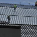 A white roof coating be applied with paint sprayers to a large commercial metal roof.