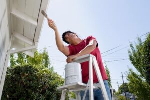 A person on a step ladder painting fascia boards.