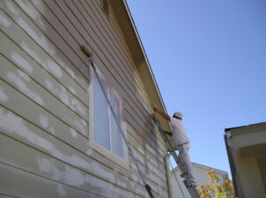 Spraying the outside siding of a house using an airless paint sprayer.